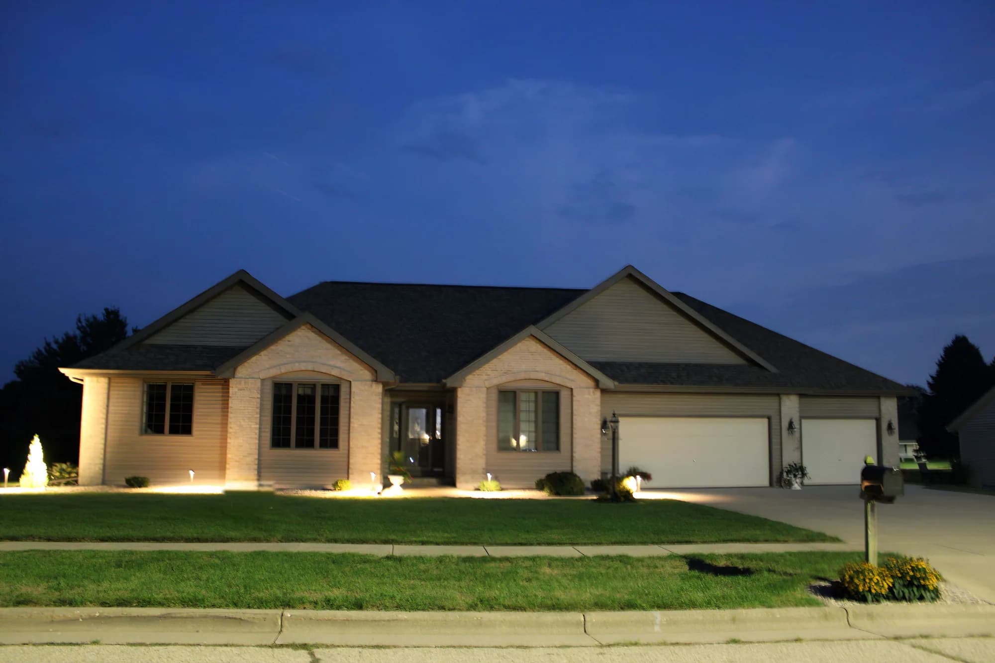 A brick ranch home at dusk with the permanent lighting switched off, showing how little the track reads when unlit