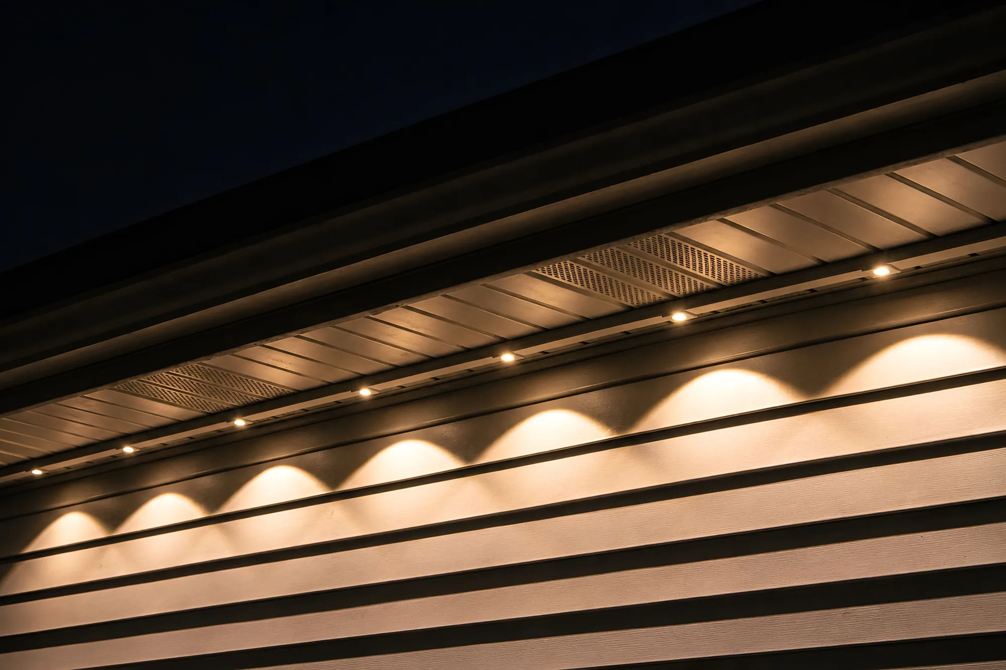 Close detail of warm-white Kussmaul Co. permanent lighting glowing along a dark soffit line