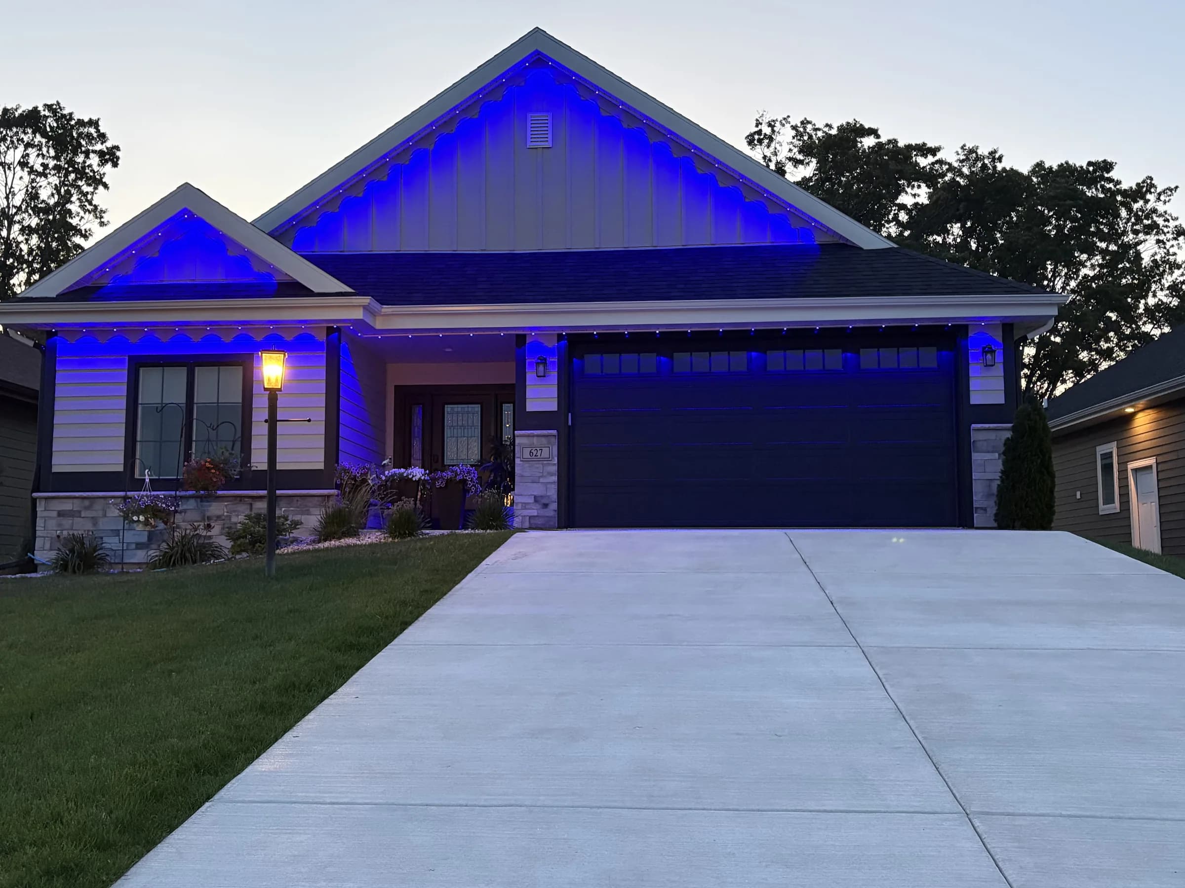 Real Kussmaul Co. permanent lighting in blue along the gables and eaves of a board-and-batten home at dusk