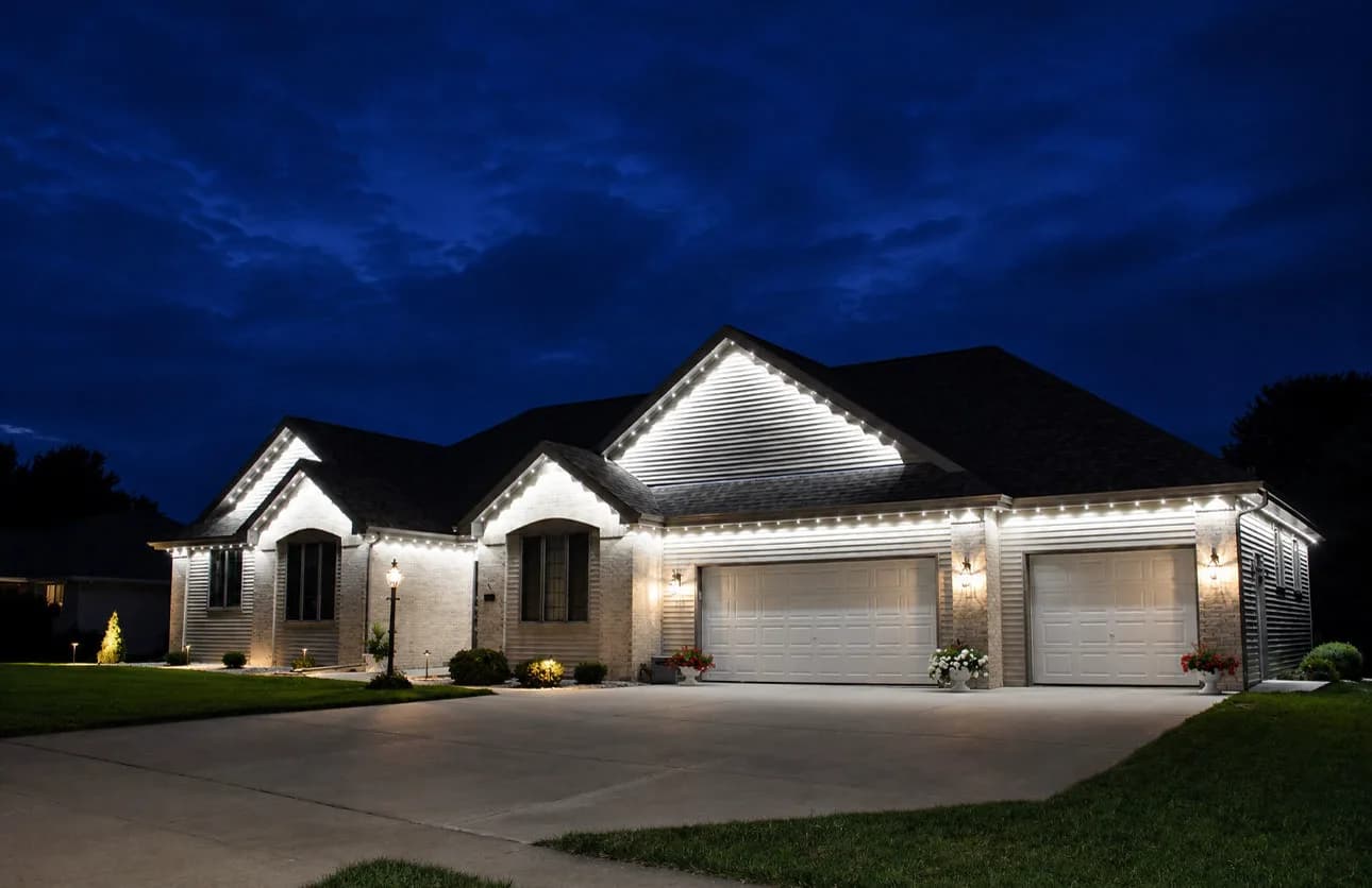 Real Kussmaul Co. permanent lighting in cool white across a three-car garage elevation, seen from the driveway