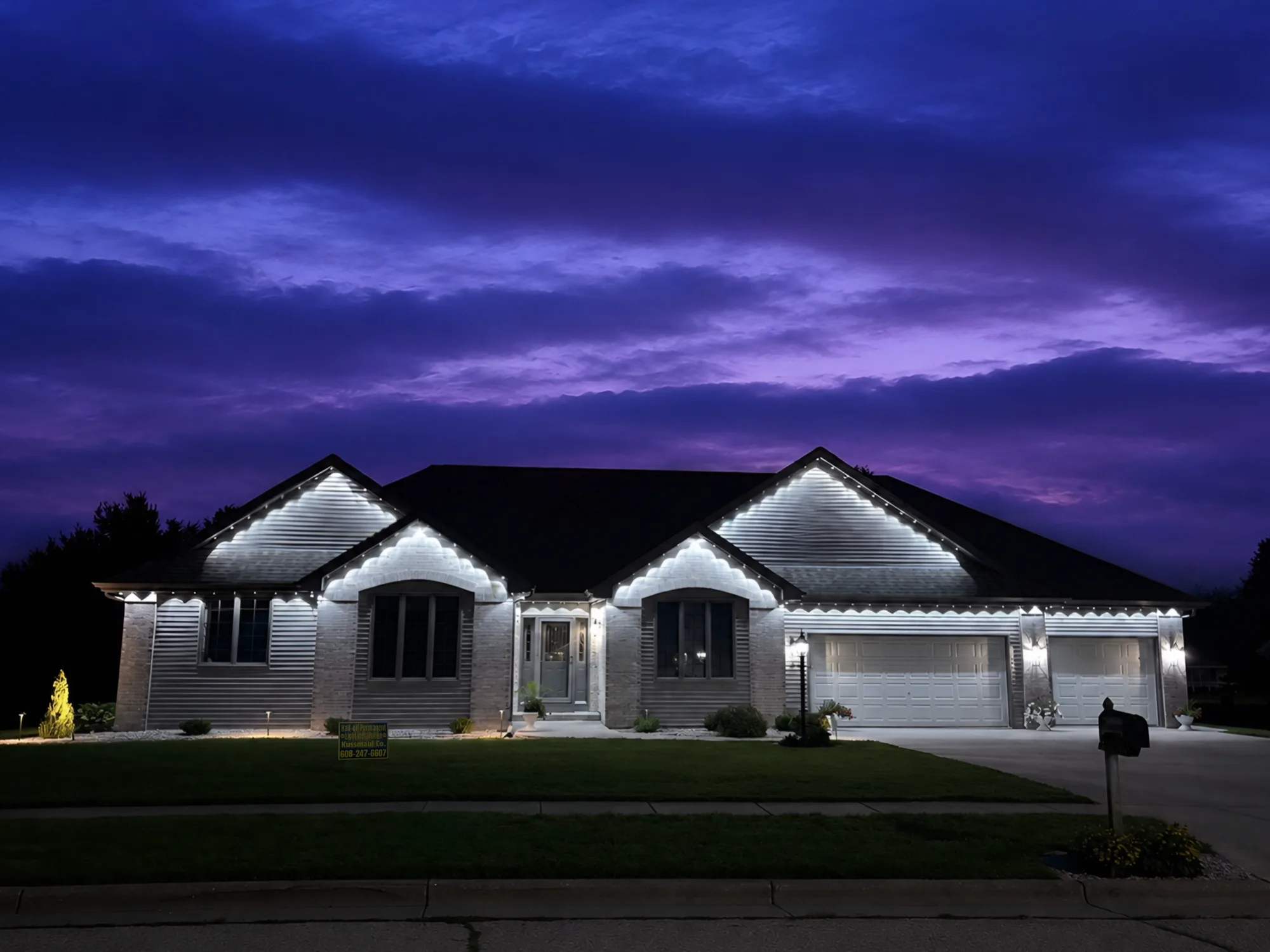 Real Kussmaul Co. permanent lighting in cool white along every gable of a brick ranch under a purple dusk sky