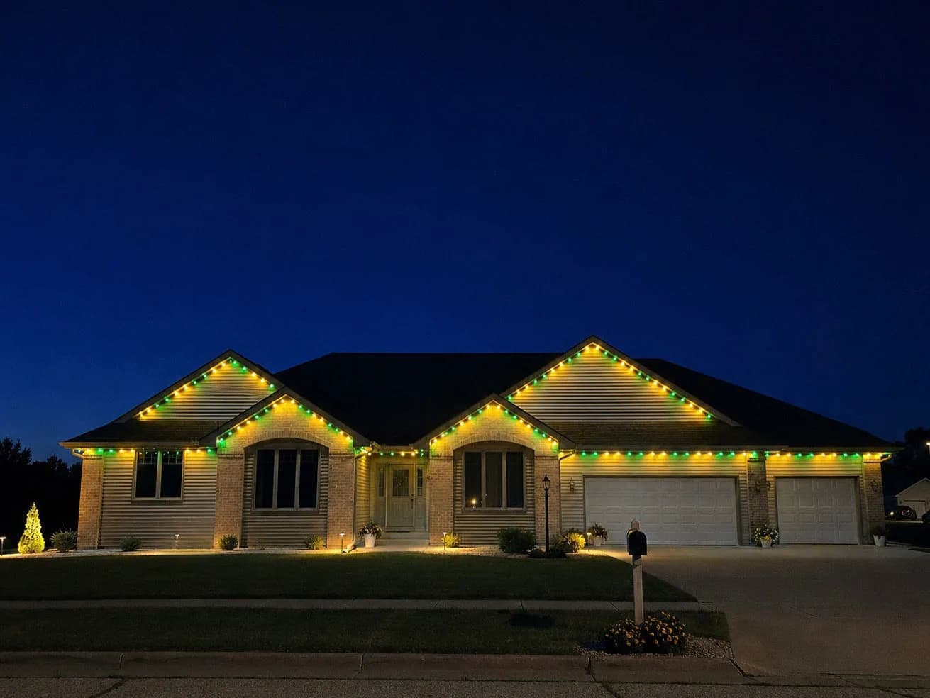 Real Kussmaul Co. permanent lighting running green and gold game-day colors across a brick ranch roofline