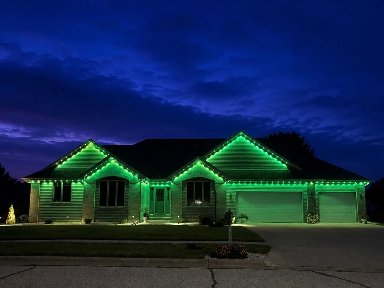 Real Kussmaul Co. permanent lighting running a full green scene across a brick ranch at dusk