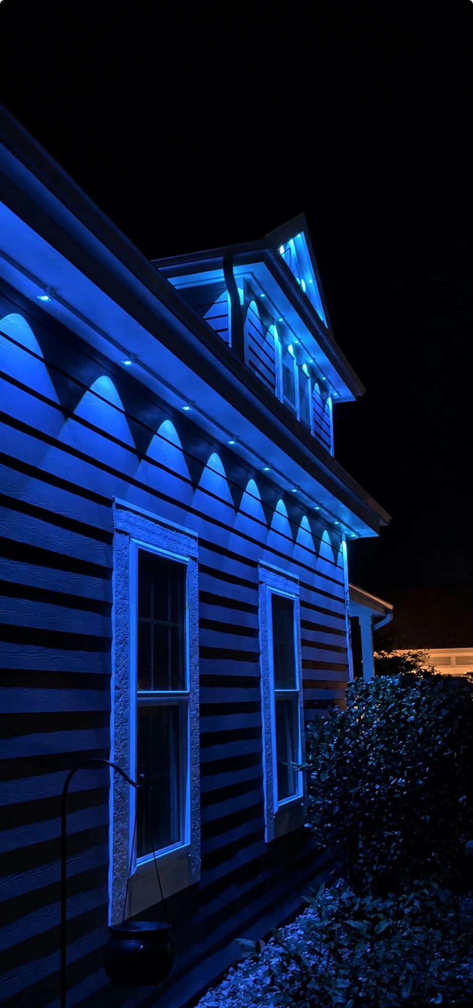 Real Kussmaul Co. permanent lighting casting even blue scallops down the siding below a roofline and dormer