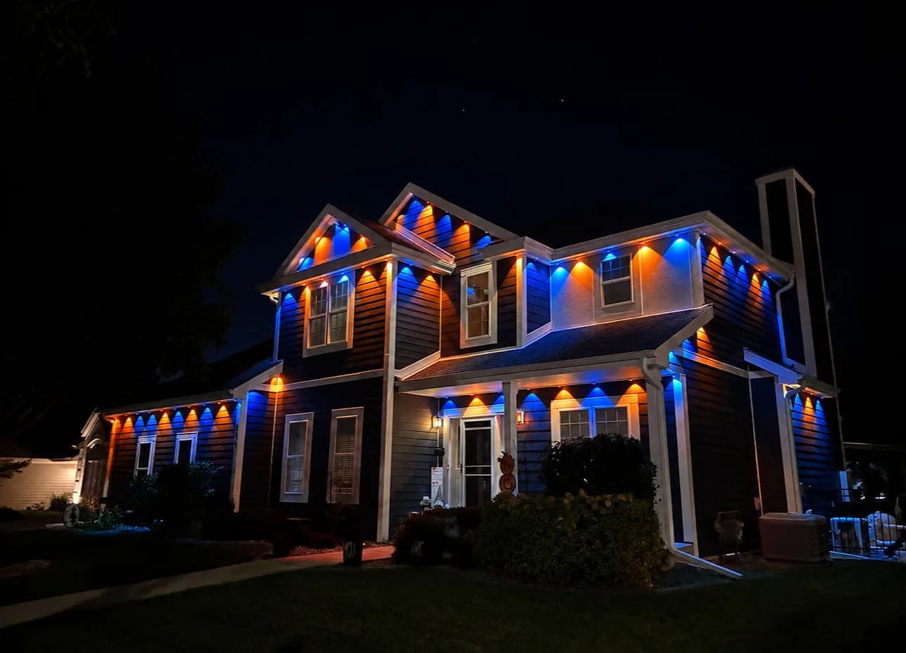 Real Kussmaul Co. permanent lighting alternating blue and orange downlights along a two-story home's rooflines
