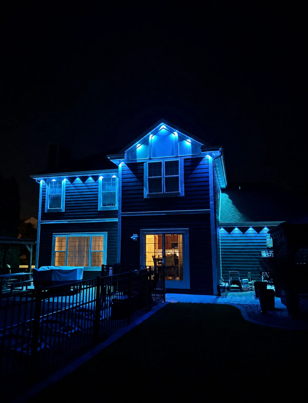 Real Kussmaul Co. permanent lighting in blue washing the back of a two-story home and its pool patio at night
