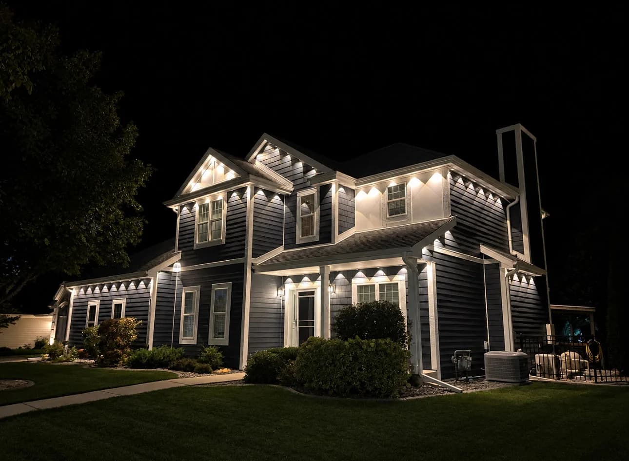 Real Kussmaul Co. permanent lighting in warm white along every gable and eave of a two-story navy home at night