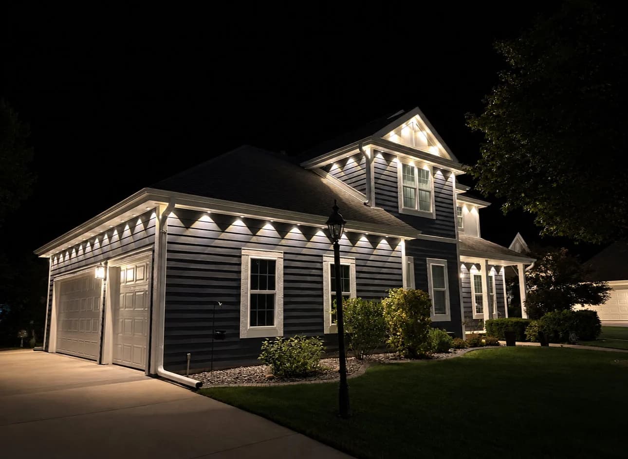 Real Kussmaul Co. permanent lighting in warm white along the garage side and front gable of a two-story home