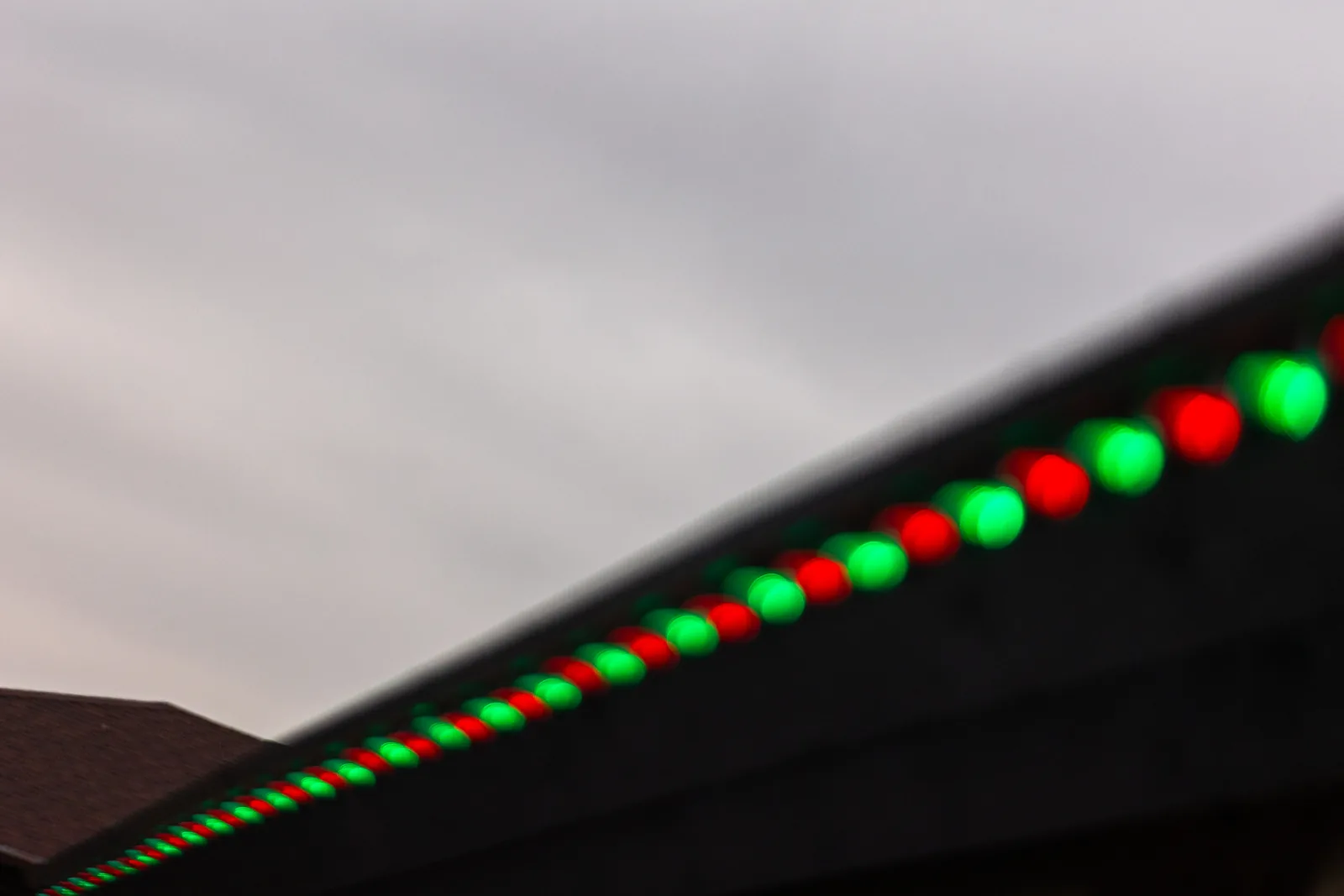 Macro detail of red and green C9 bulbs clipped to a roofline for a real Kussmaul Co. holiday lighting install