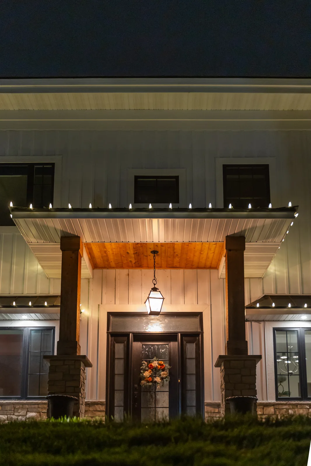 Close-up of a real Kussmaul Co. holiday lighting install: a hanging lantern, wreath on the door, and warm C9 lights along a farmhouse entry