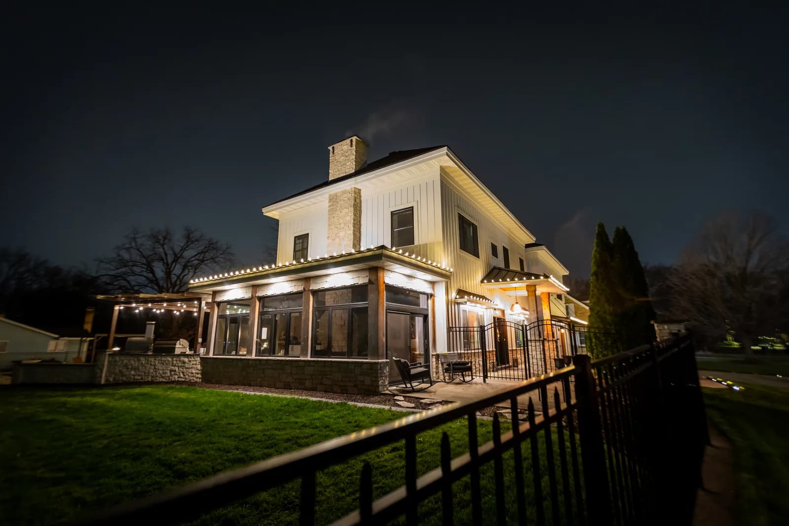 Rear patio and screened porch with warm white roofline lighting and string lights over outdoor kitchen