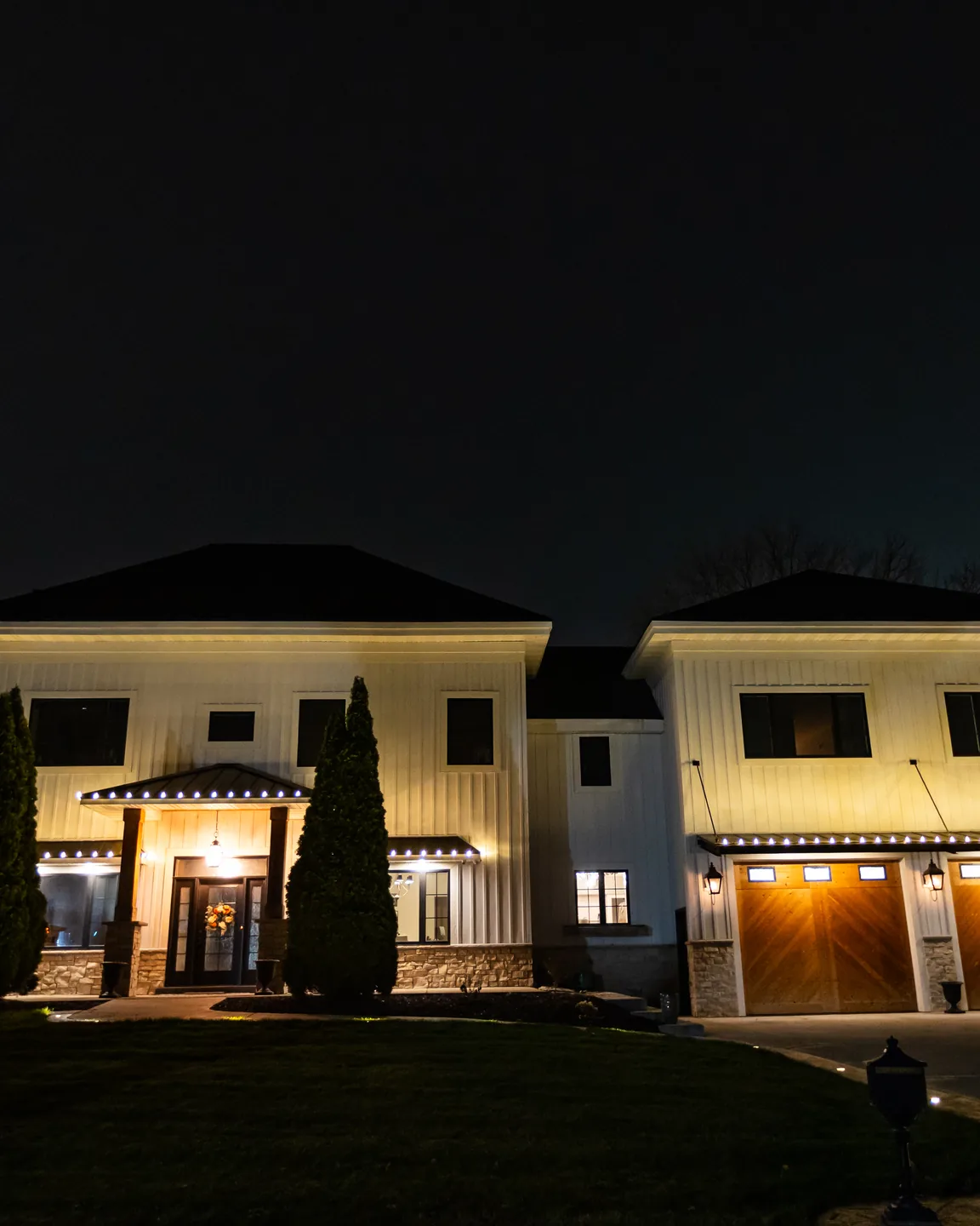 Real Kussmaul Co. holiday lighting installation glowing warm white along the eaves of a large home at night