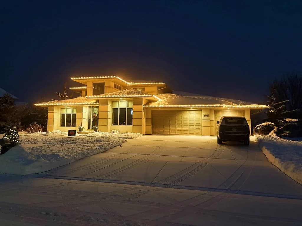 Two-story stucco home with warm white roofline lighting on snowy winter evening
