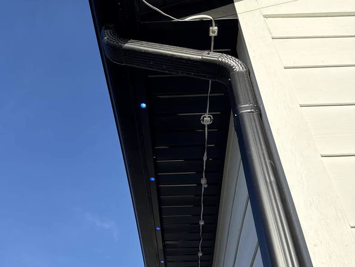 A permanent lighting cord clipped directly to a dark soffit, with white cord and white plastic clips clearly visible in daylight and sagging between fixings