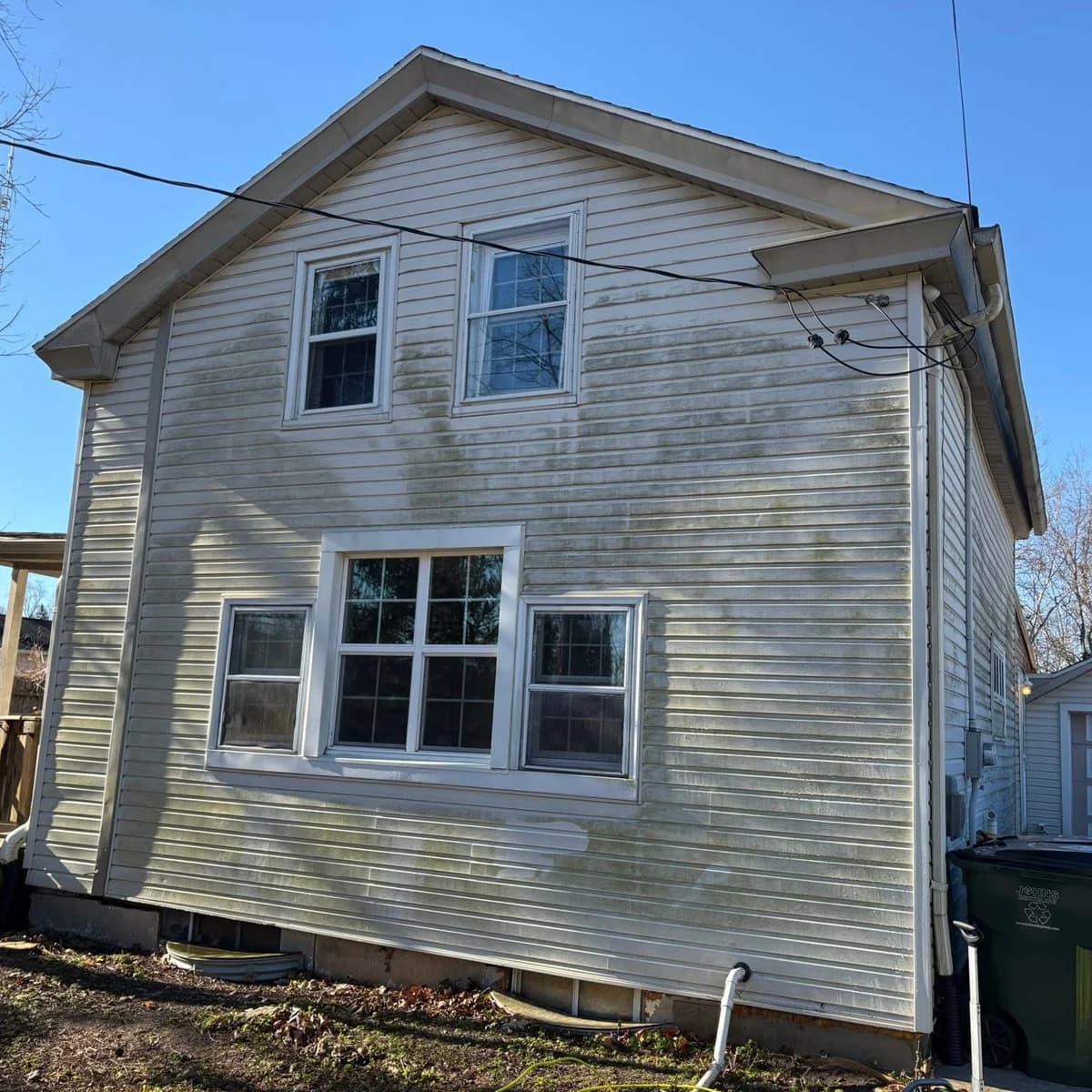 A two-story home with its vinyl siding streaked green with algae before a Kussmaul Co. soft wash