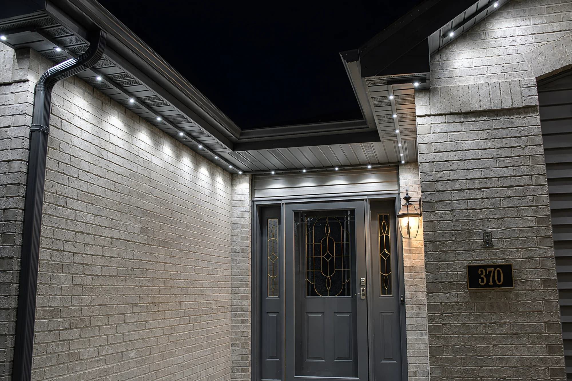 Soffit-mounted track at night, throwing even points of light down a brick entryway