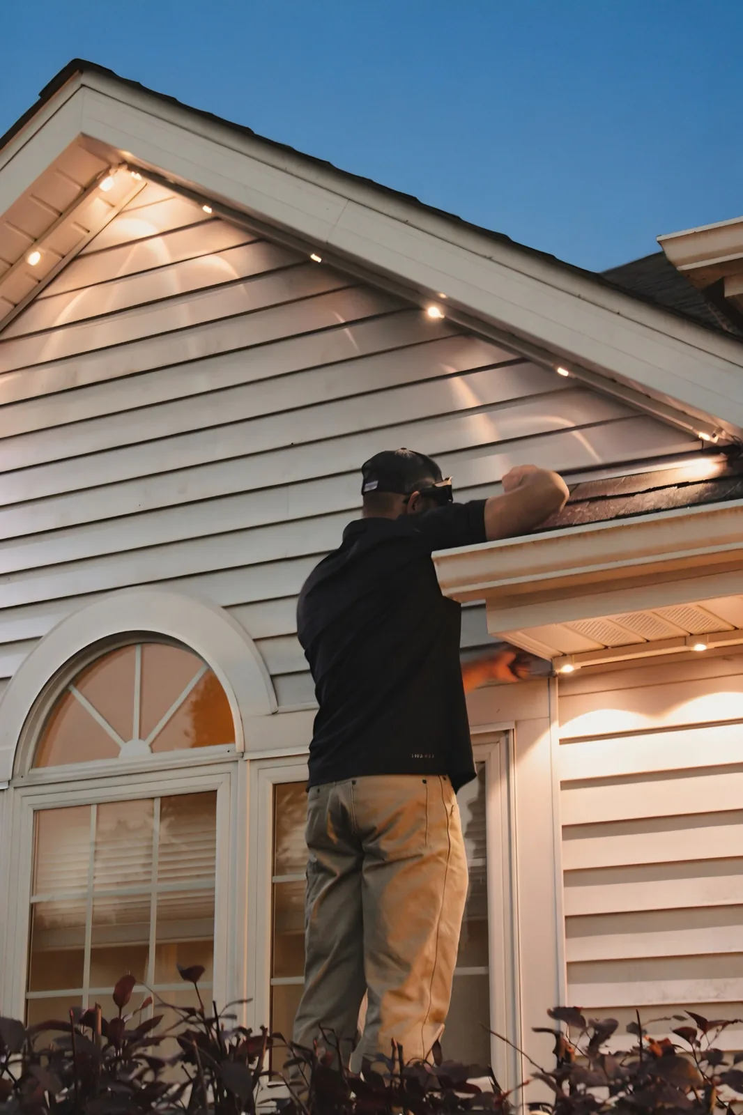 Kussmaul Co. installer working a warm-white roofline install at dusk