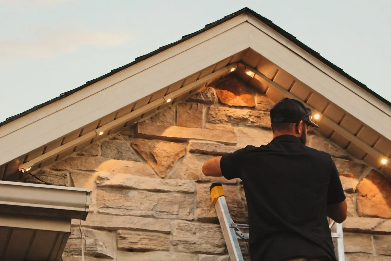 Kussmaul Co. installer fitting permanent lighting track on a stone gable at golden hour