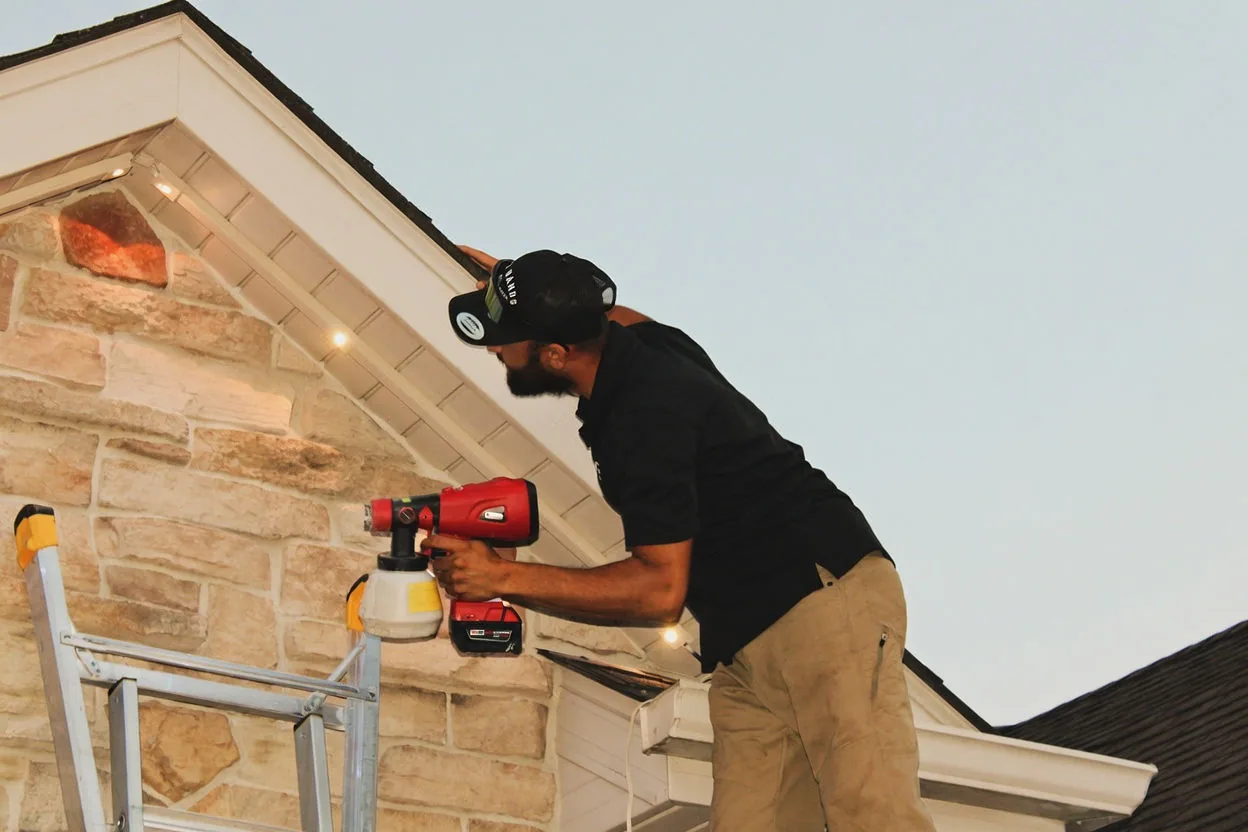 A Kussmaul Co. installer spray-painting a run of lighting track to match the home's white soffit before mounting it