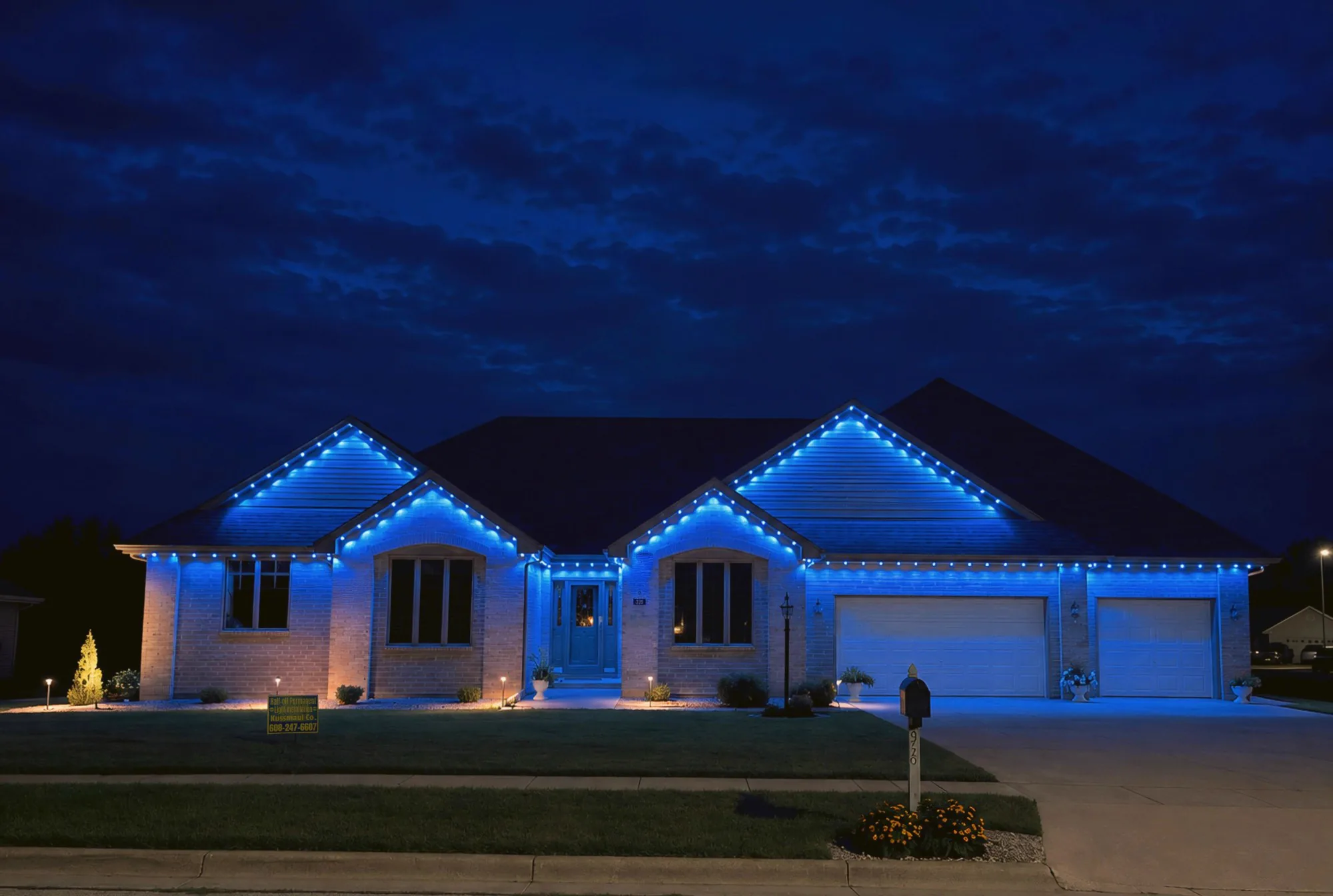Real Kussmaul Co. permanent lighting running a full blue scene across a brick ranch home's roofline and three gables at dusk