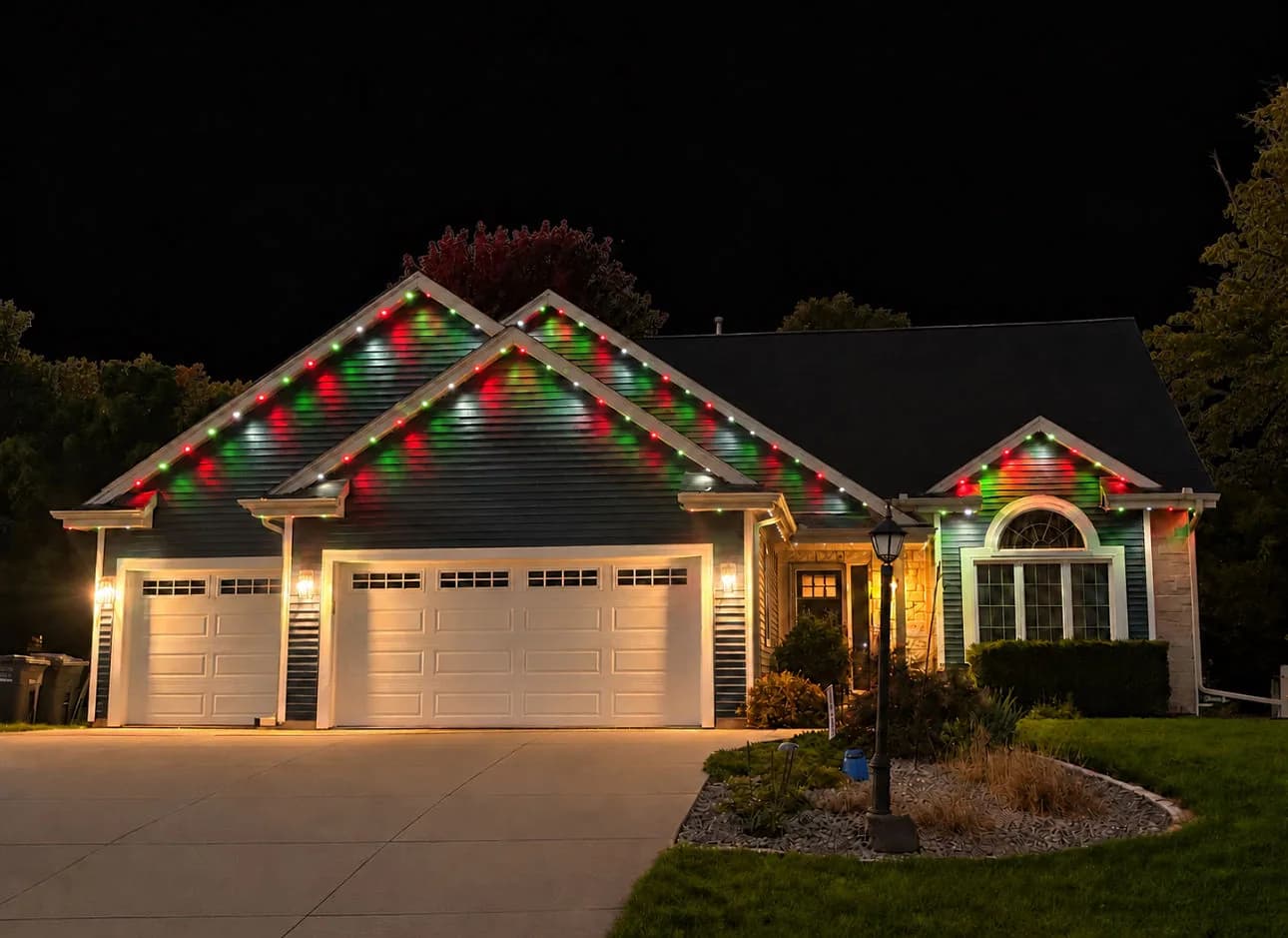 Real Kussmaul Co. permanent lighting running a red and green Christmas scene across a ranch home's gables and three-car garage