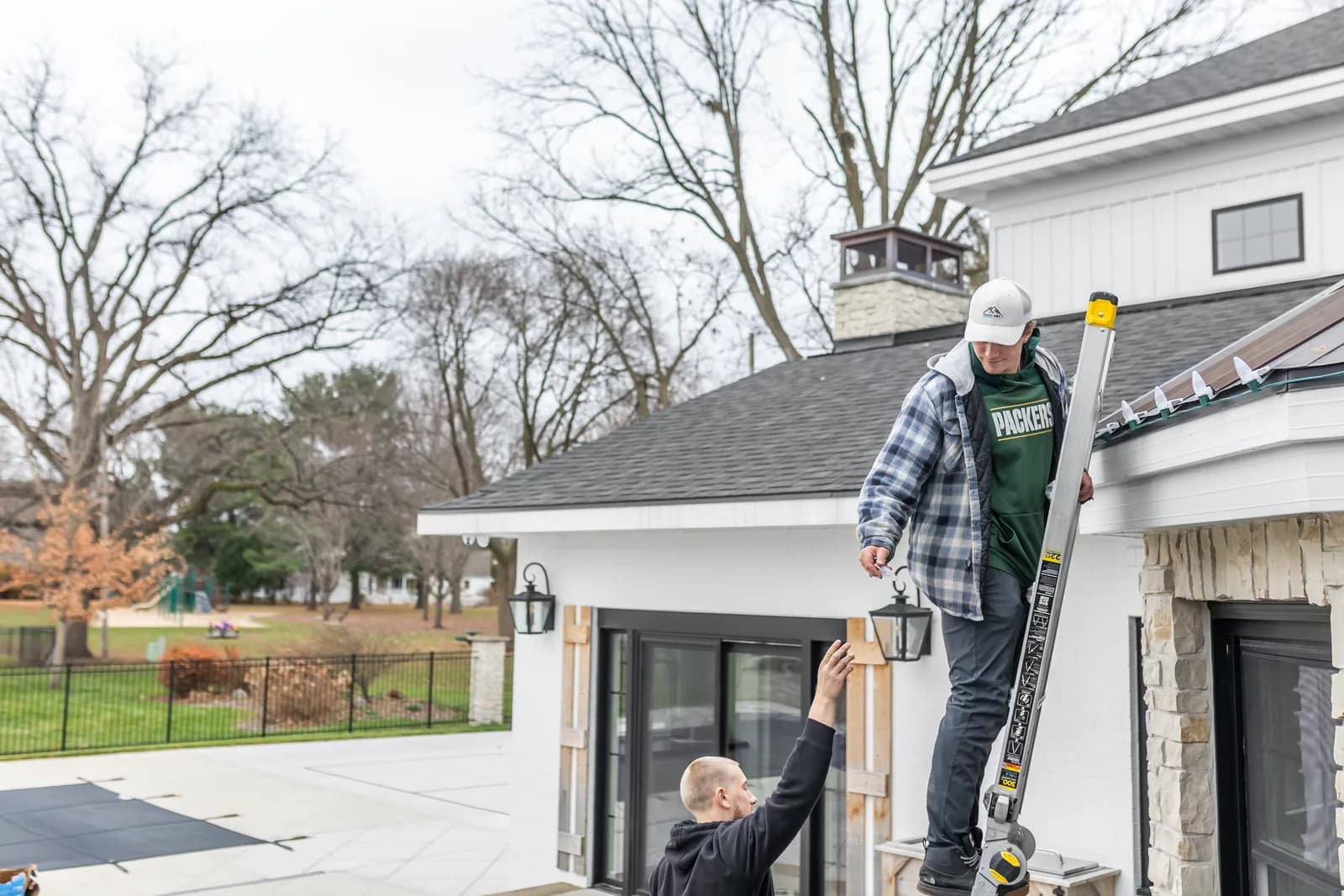 Real Kussmaul Co. crew installing holiday lights on a white farmhouse roofline by daylight, working from a ladder